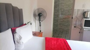 A hotel room with a bed, a fan, a microwave, and a door leading to another room. - Neo & Ruks Guest House Parow (Cape Town)