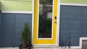 A house with a yellow door, green and blue siding, a potted plant, and a small garden area. - Charming 2-bedroom house in beautiful Somers with AC (Somers)