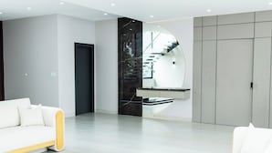 A modern living room with a white sofa, a round mirror, and a staircase with a glass railing. - La Vie Es Belle Beach House (Santa Eleana)
