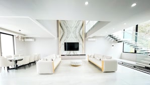A spacious living area with a large TV, white sofas, and a marble-patterned wall. - La Vie Es Belle Beach House (Santa Eleana)