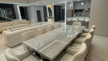 Un vaste espace dédié à la salle à manger, avec une longue table et de nombreuses chaises, une cuisine équipée d’appareils modernes, et un escalier menant à l’étage supérieur.