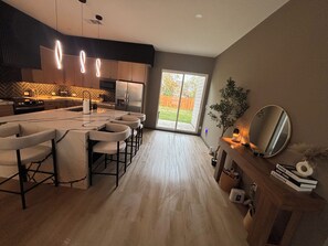 Una cocina moderna con una isla central, taburetes de bar y un área de comedor con un amplio ventanal.