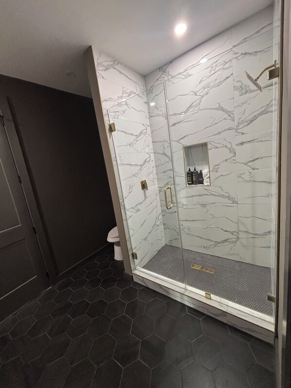 Un baño moderno con ducha de vidrio, paredes de mármol y un patrón de suelo hexagonal.