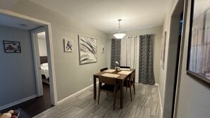 A dining area with a wooden table and chairs, a ceiling light, and a view of a bedroom through an open door. - Charming duplex - convenient, comfortable, Close to It All. Beach, Work & Play! (Corpus Christi)