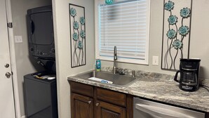 A kitchen with a dishwasher, a coffee maker, and a window with blinds. - Charming duplex - convenient, comfortable, Close to It All. Beach, Work & Play! (Corpus Christi)