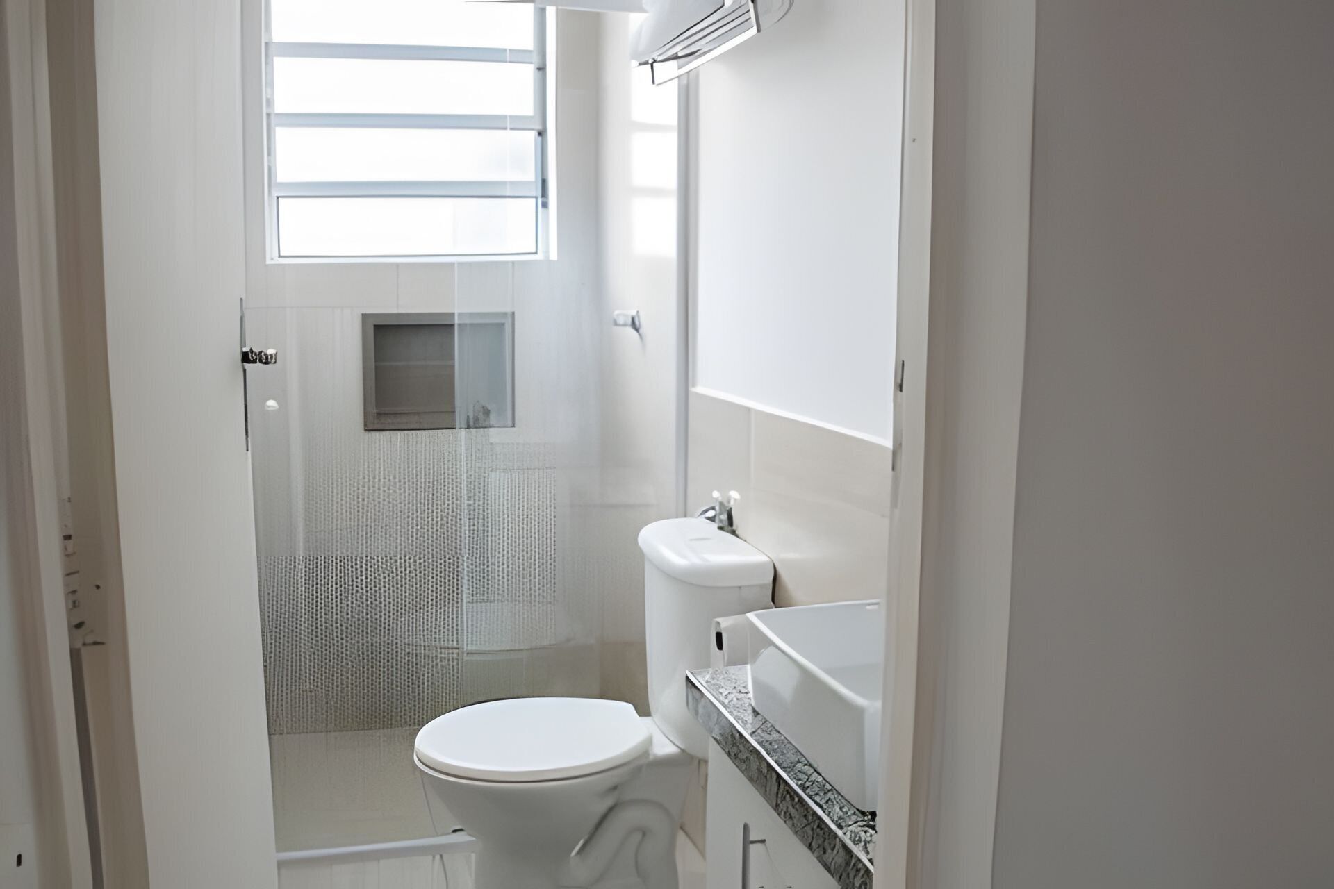 A bathroom with a toilet, sink, and mirror. There is a window with blinds above the toilet.