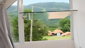 Quarto com uma grande janela com vista para uma paisagem verde e uma colina distante.