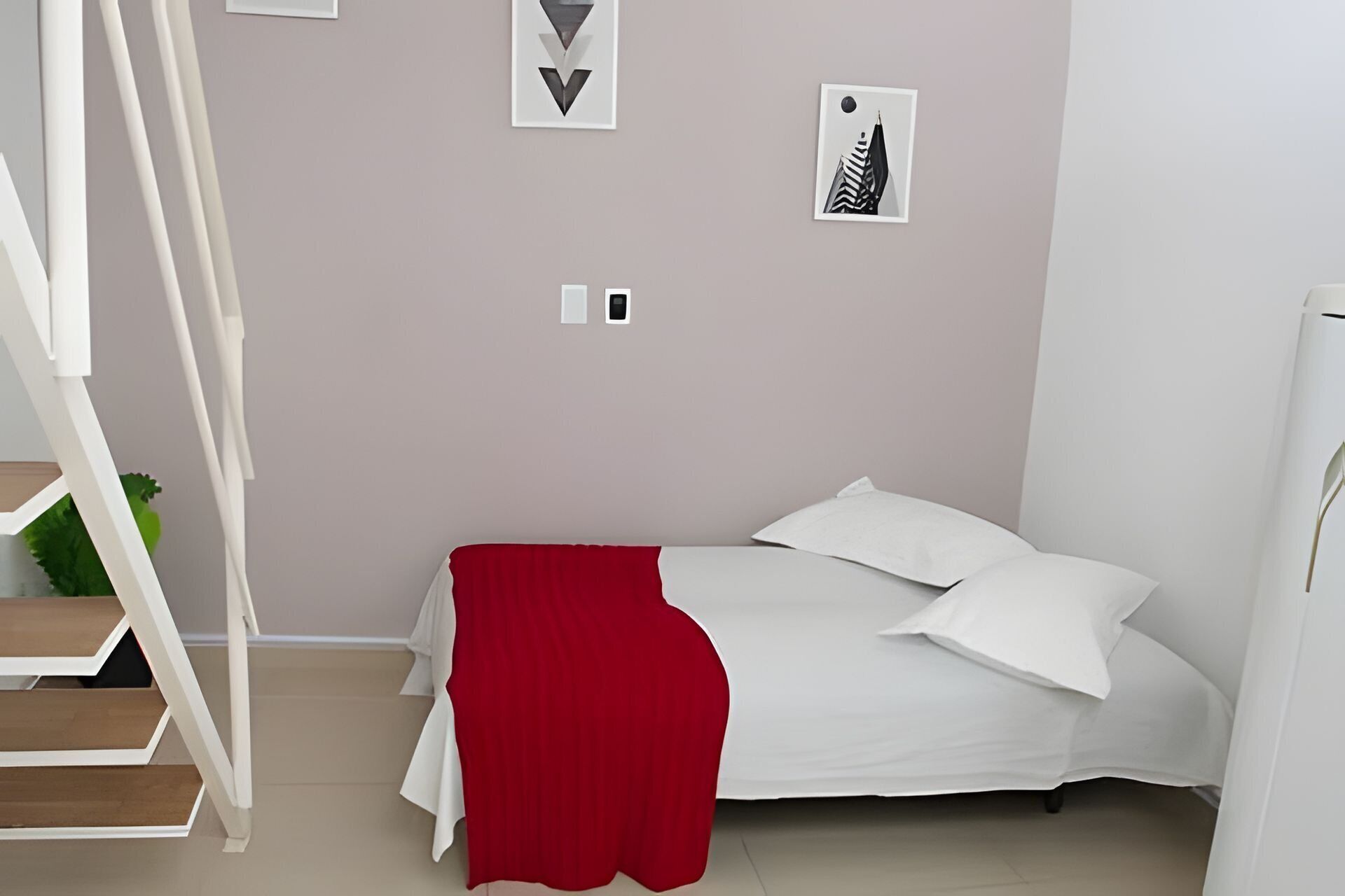 A bedroom with a bed, white pillows, a red throw, a staircase, and a wall with framed pictures.