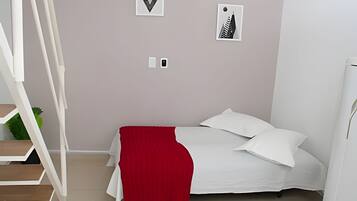 A bedroom with a bed, white pillows, a red throw, a staircase, and a wall with framed pictures.