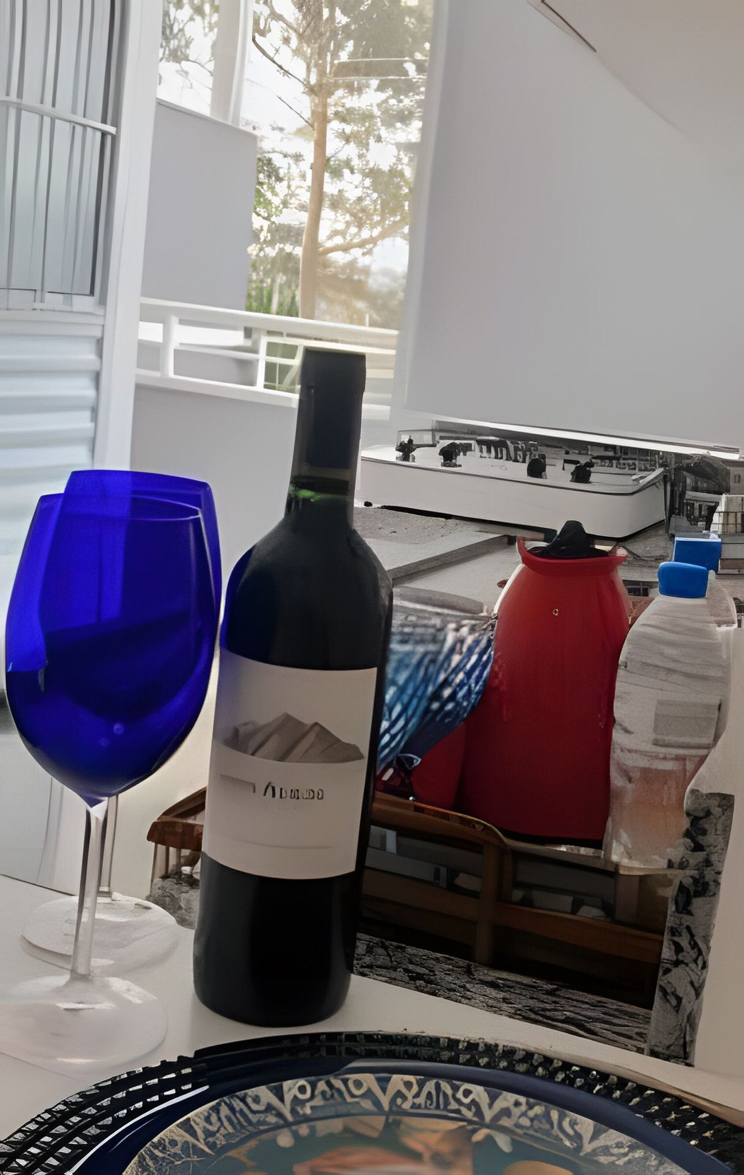 Una botella de vino y una copa sobre una mesa, con vista a un balcón y mobiliario exterior.