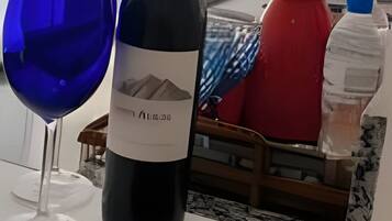 Una botella de vino y una copa sobre una mesa, con vista a un balcón y mobiliario exterior.