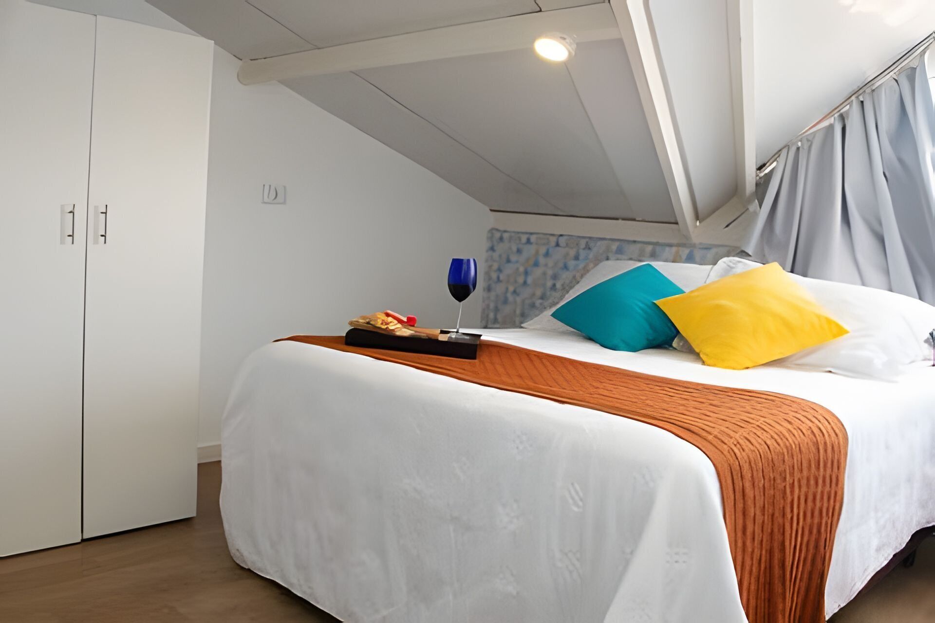 Un dormitorio con una cama, una mesita de noche con una copa de vino y una mesita auxiliar.