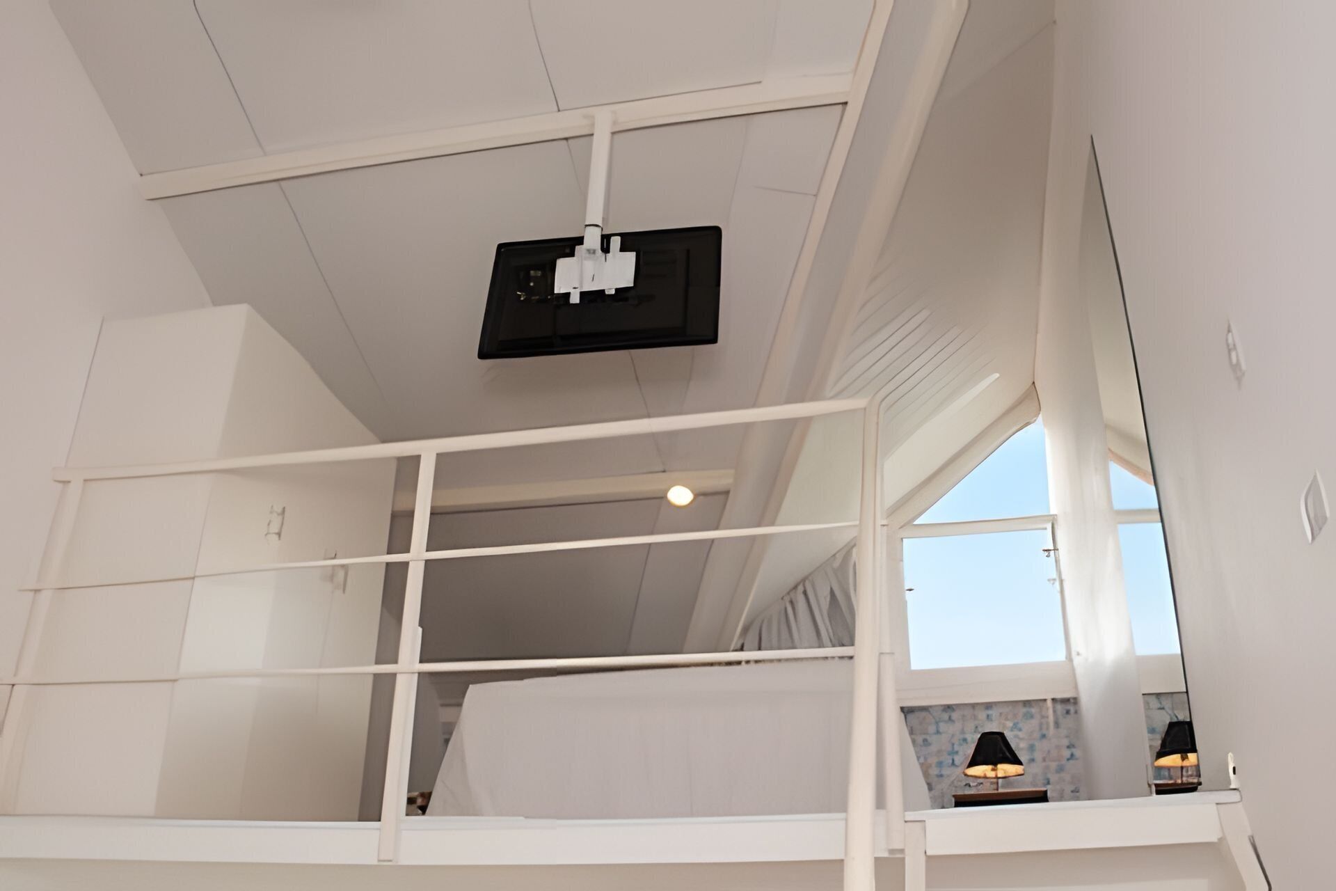 Quarto com beliche, televisão instalada no teto, janela e abajur na mesinha de cabeceira.