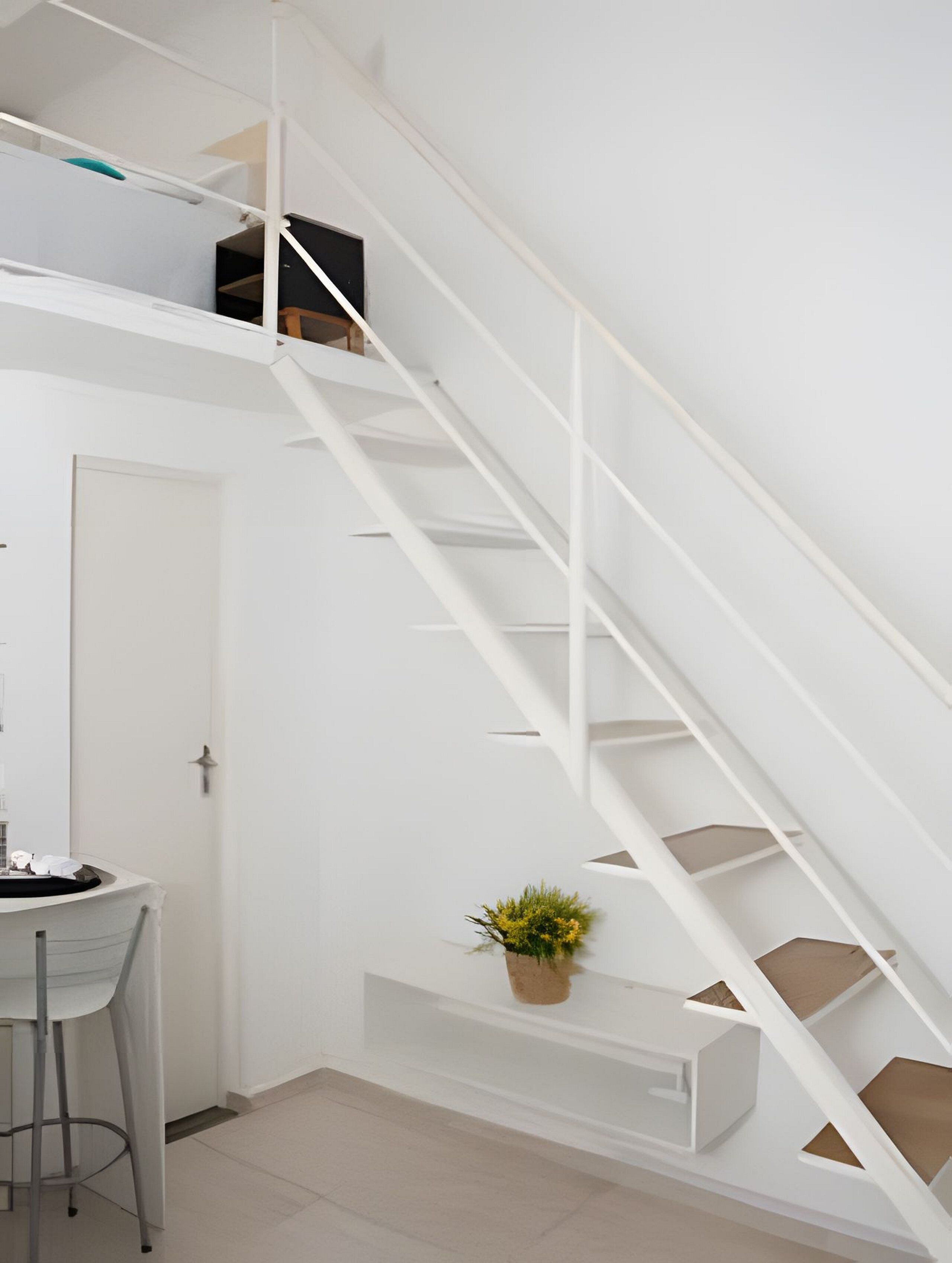A white staircase with a handrail, a small potted plant on the landing, and a desk with a chair in the foreground.