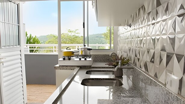 Cozinha moderna com uma grande janela, bancadas de granito, pia e painel com padrões geométricos.