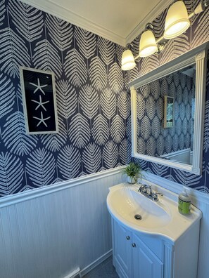 Une salle de bain avec un papier peint à motifs, un lavabo, un miroir et un tableau encadré accroché au mur.