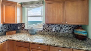 Eine Küche mit Holzschränken, einer Granit-Arbeitsplatte und Blick aufs Meer.
