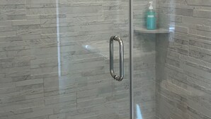 A glass-enclosed shower area with a tiled floor and a shelf with toiletries.