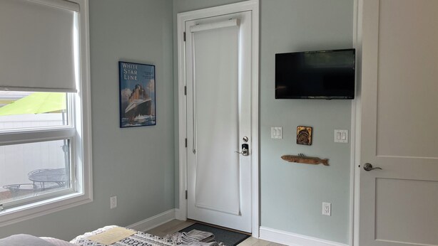 A hallway with a white door, a mounted television, a framed picture of a ship, and a small decorative item on the wall.