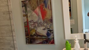 A bathroom with a toilet, a sink, a mirror, and a painting on the wall.