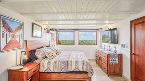 Une chambre à coucher avec un lit, des tables de chevet, une commode et un téléviseur fixé au mur.