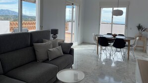 A modern living room with a grey sofa, a dining table with chairs, and large windows offering a view of the outdoors. - Penthouse with exceptionel sea, mountain and golf view over Miraflores golf (AN)