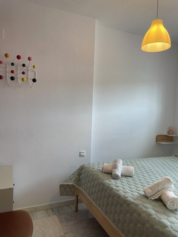 Una camera da letto con un letto, un lampadario, un'opera d'arte colorata a parete e un piccolo ripiano con un oggetto decorativo.