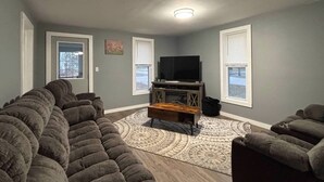 Ein Wohnzimmer mit einem Ecksofa, einem Fernseher auf einem Holzboden und einem gemusterten Teppich.