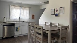 Eine moderne Küche mit Geschirrspüler, Spüle und einem Essbereich mit Tisch und Stühlen. An der Wand befinden sich gerahmte Zertifikate.
