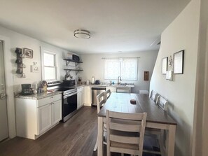A compact kitchen with white cabinets, a dining table with chairs, and a window with curtains.