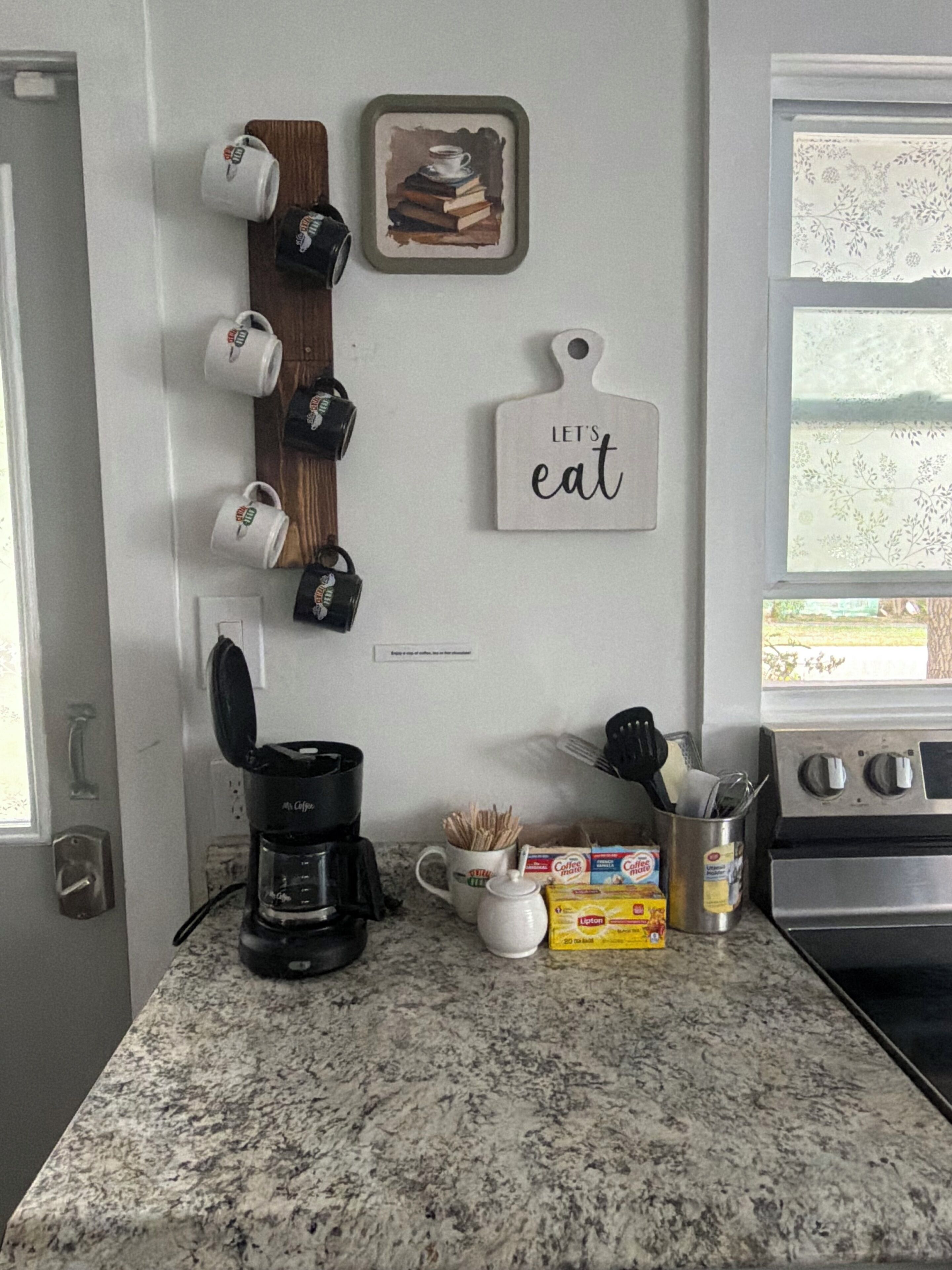 Eine Küche mit Kaffeemaschine, Tassen, einer Kaffeetasse, einem Toaster, einer Packung Lipton Tee und einem Herd.