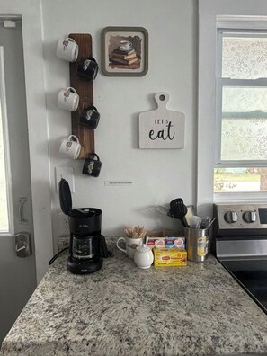 A kitchen with a coffee maker, mugs, a coffee cup, a toaster, a box of Lipton tea, and a stove.
