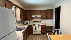 Une cuisine compacte avec des meubles de rangement en bois, un réfrigérateur blanc, un four à micro-ondes, un four traditionnel et une table à manger en bois avec des chaises.