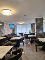 Un restaurante moderno con suelo de mármol, asientos tapizados en negro y una pantalla de televisión en la pared.