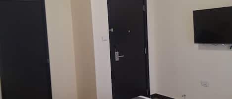 A hotel room with a bed, a television mounted on the wall, and two doors.