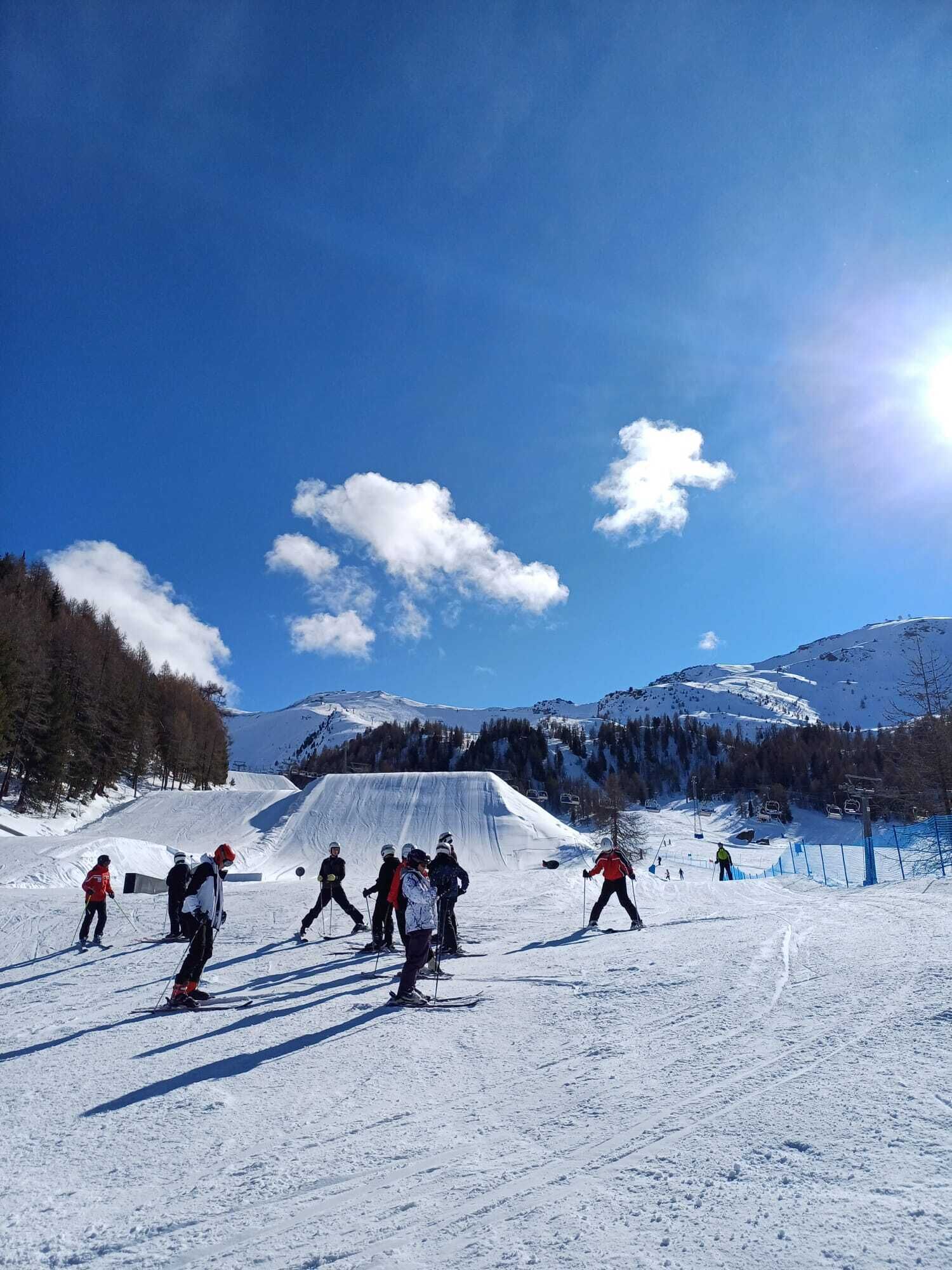 A ski slope with skiers, a clear sky, and snow-covered mountains.
