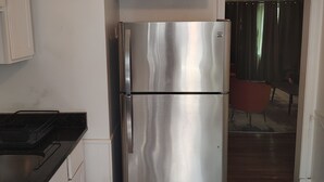 A kitchen with a stainless steel refrigerator, white cabinets, and a black countertop.