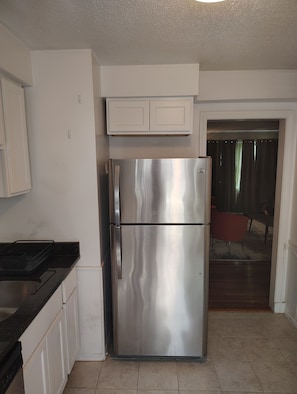 A kitchen with a stainless steel refrigerator, white cabinets, and a black countertop.