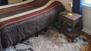 A bedroom with a bed, a bedside table with a lamp, a wall with decorative words, and a window with curtains.