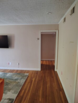 Una stanza con pavimento in legno, una TV a schermo piatto montata sulla parete e una porta che conduce a un'altra stanza.