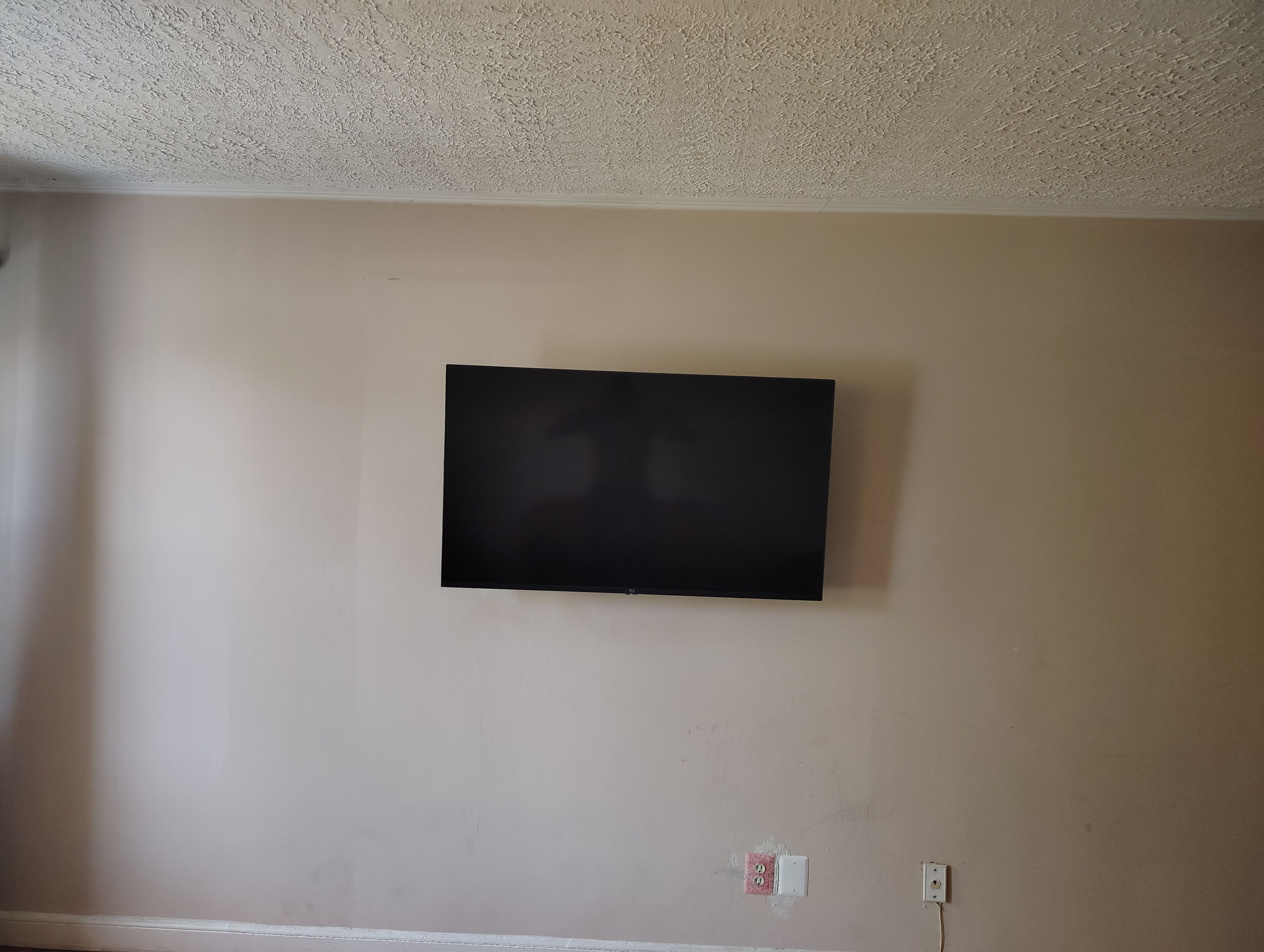 Una habitación con una televisión de pantalla plana montada en la pared, un zócalo blanco y un enchufe.