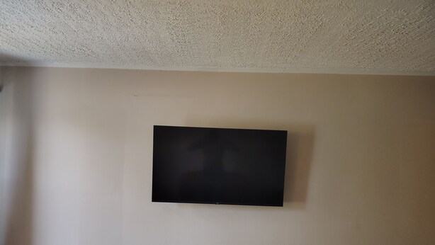A room with a flat-screen TV mounted on the wall, a white baseboard, and a power outlet.