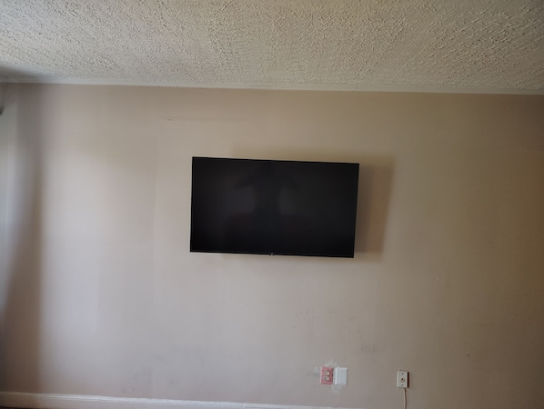 A room with a flat-screen TV mounted on the wall, a white baseboard, and a power outlet.