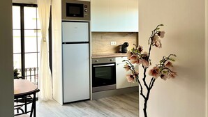 Una cocina moderna con microondas, horno y refrigerador integrados. Cuenta con una zona de comedor con mesa y sillas, además de una planta en maceta con flores.
