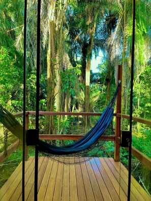 A hammock on a wooden deck surrounded by dense tropical foliage.