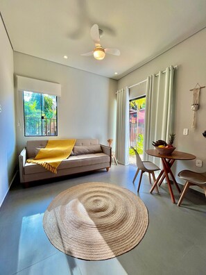 A modern living room with a sofa, a round rug, a dining table with chairs, a ceiling fan, and a window with curtains.