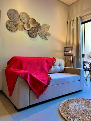 A living room with a sofa, a red throw blanket, a woven wall art piece, a floor lamp, and a round woven rug.