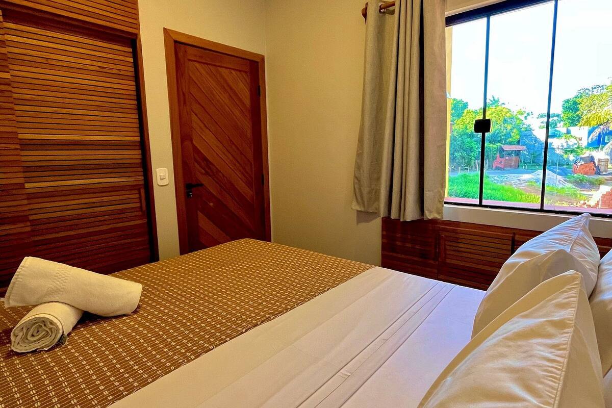 Une chambre d’hôtel avec un lit, une porte en bois, une fenêtre avec des rideaux et une vue sur la verdure.