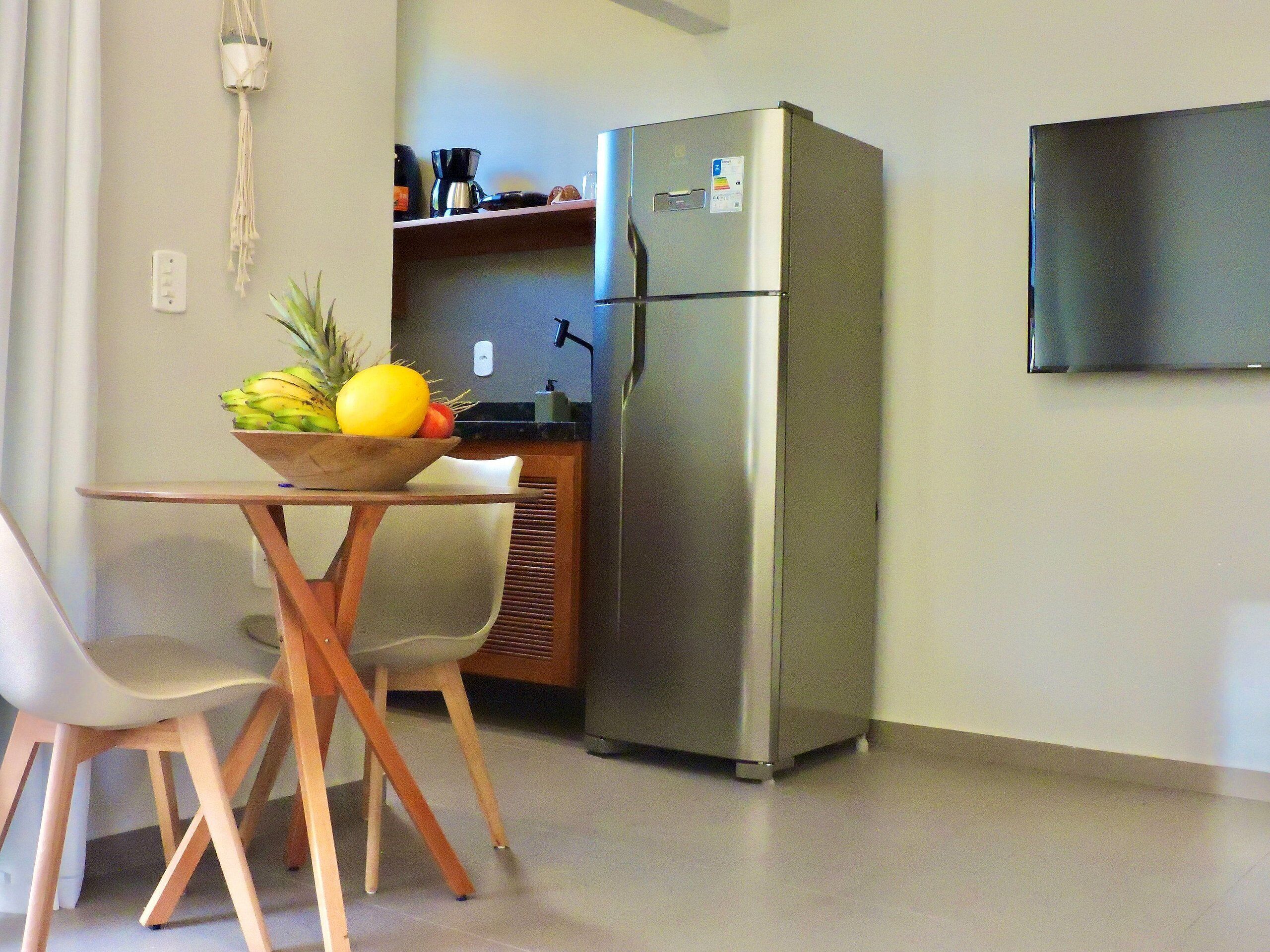 Una kitchenette compacta con un refrigerador de acero inoxidable, una pequeña encimera y un bol de fruta sobre una mesa.
