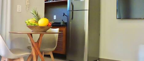 Una kitchenette compacta con un refrigerador de acero inoxidable, una pequeña encimera y un bol de fruta sobre una mesa.
